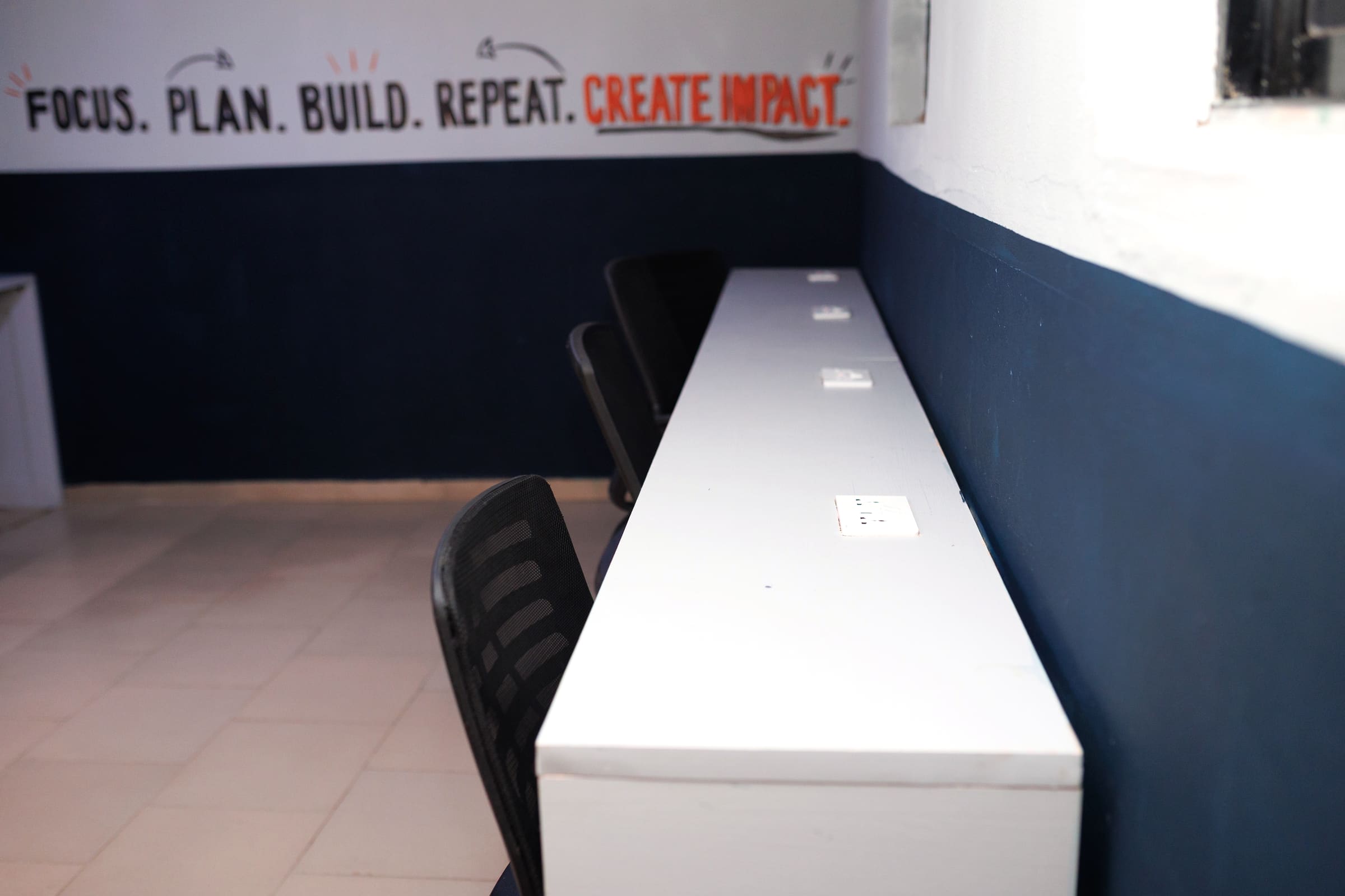 A long white desk against a navy wall, with a power socket set into the wall beside each seat.
